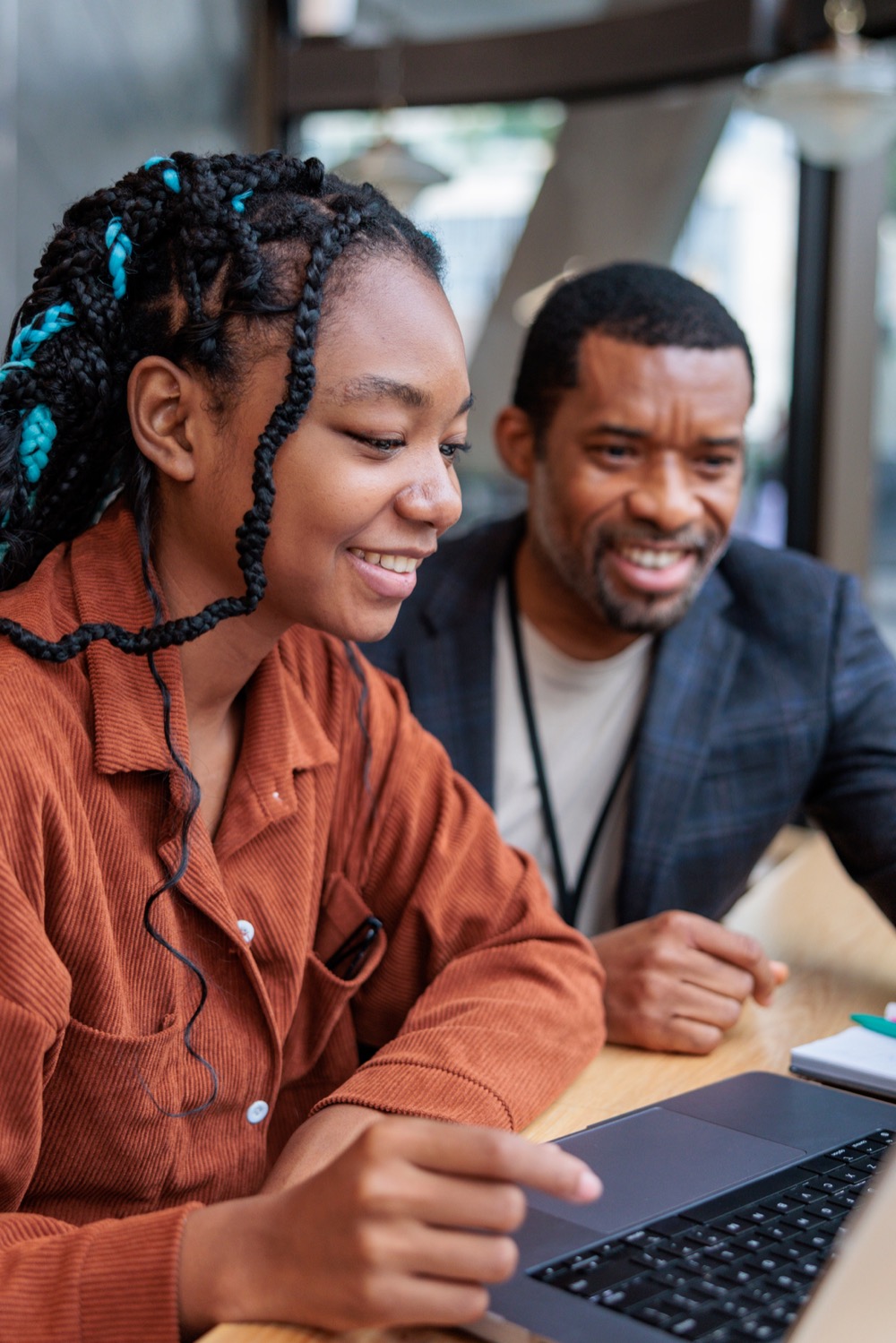 A student with teal braids and an adult mentor smiling at a laptop together